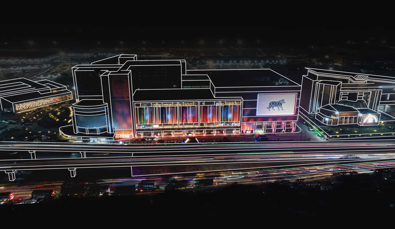 Aerial night view of Centrepoint Dhaka shopping mall with illuminated storefronts and light-trail traffic in front